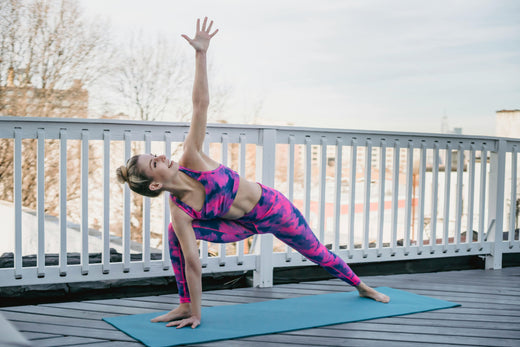 A woman practicing Extended Side Angle Pose (Utthita Parsvakonasana) on a rooftop yoga mat, showcasing flexibility and strength against a beautiful urban skyline background.