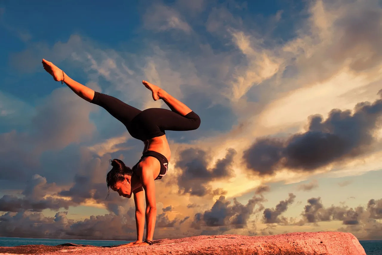 A woman performing a handstand yoga pose at sunset