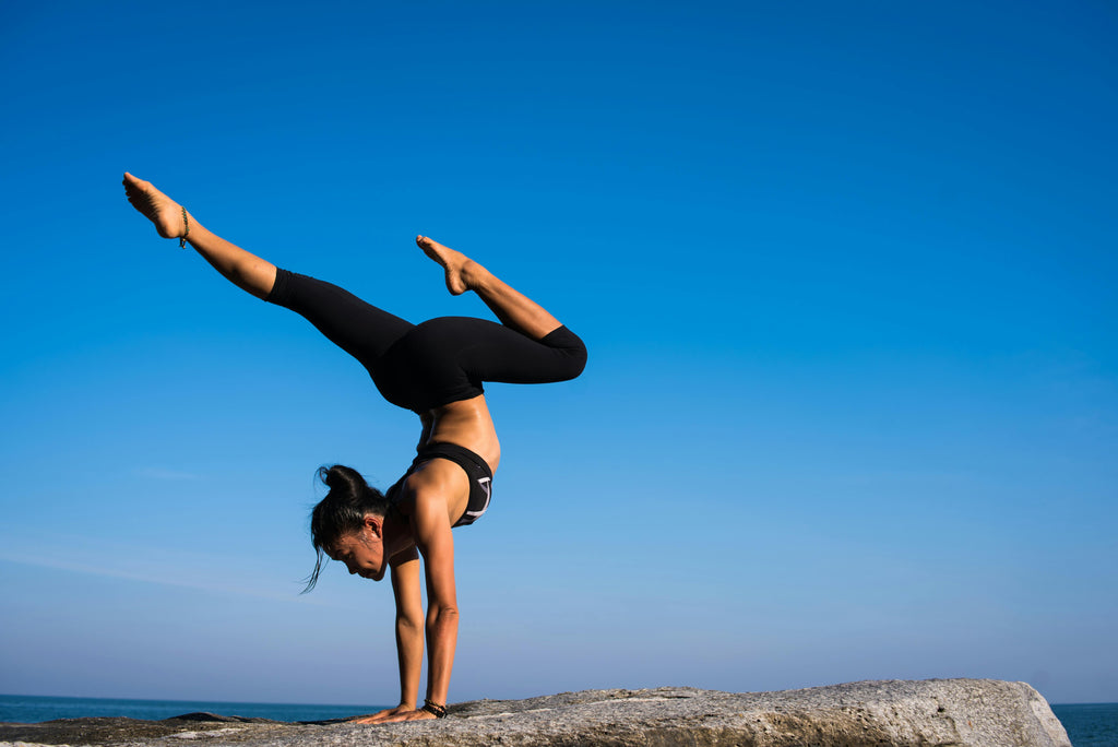 A woman practicing a yoga handstand pose on a rock against a stunning blue sky. Perfect for fitness, yoga, and mindfulness inspiration.