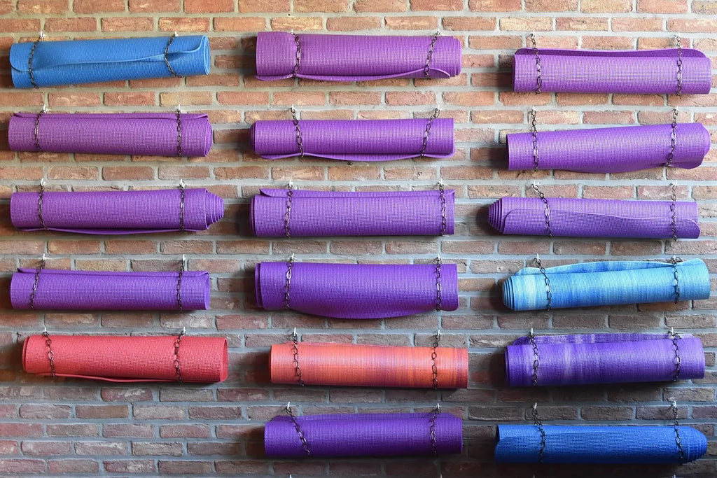 Multiple rolled yoga mats in blue, purple, and red colors hanging on a brick wall.