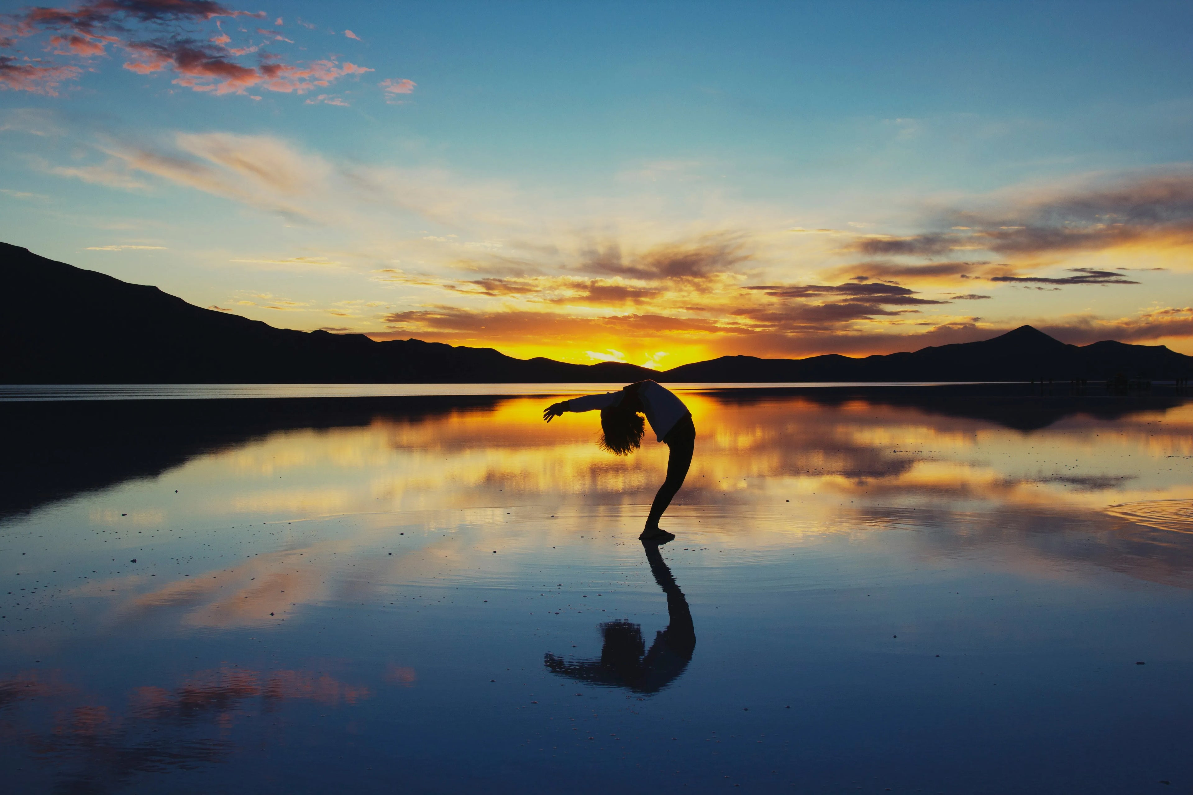 A girl exercising at sunset on a mirrored water surface reflecting the sky