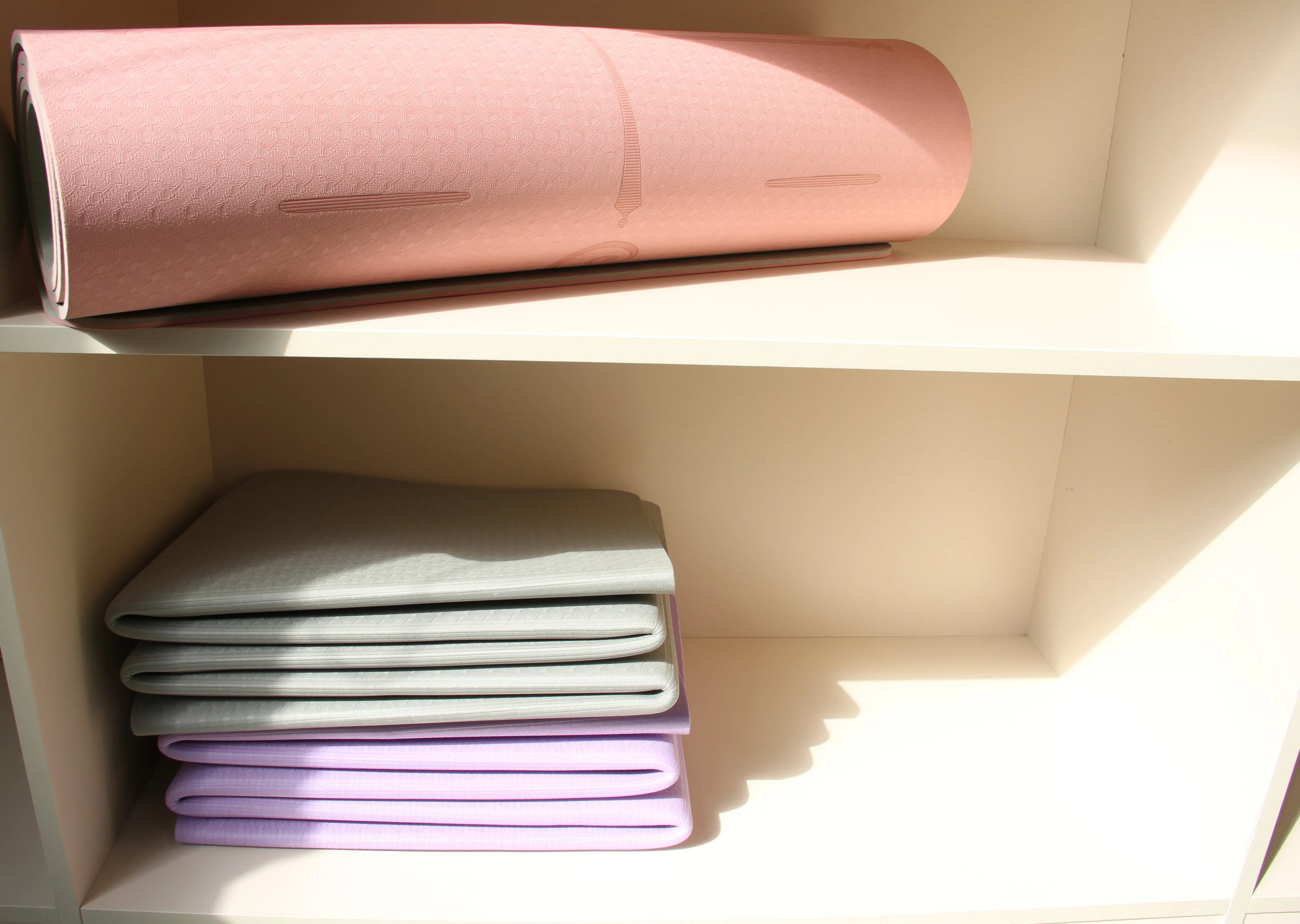 Sportive Lives pink yoga mat and foldable gray and purple mats, neatly stored for home or studio use in Canada.