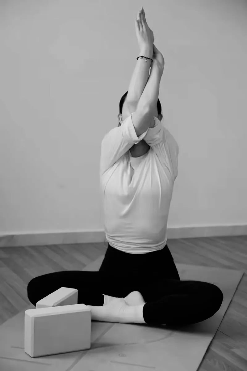 Woman in a seated position with Eagle Arms, yoga blocks resting beside her for potential support.